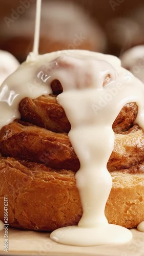 White icing flowing down a freshly baked cinnamon roll with steam rising in a cozy bakery