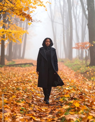 Woman in Black Coat Walking Through Autumn Forest Path Covered in Leaves
