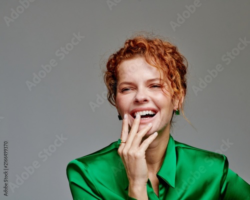Fotografía Joyful Woman Smiling in a Green Satin Blouse with Curly Hair Against a Neutral B