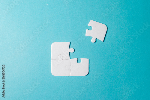 Fotografie Three connected white jigsaw puzzle pieces with one separate piece remaining to be fitted on blue