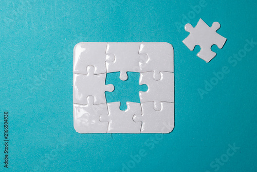 Konstfotografi White jigsaw puzzle missing its center piece with the final piece placed nearby on a blue background