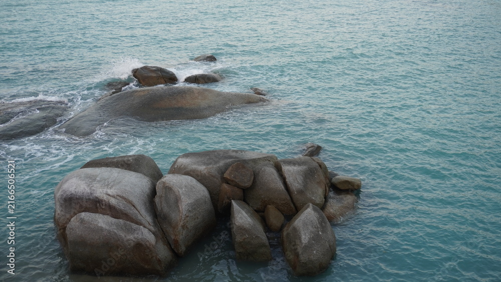 Fototapeta premium High angle view of large granite boulders sitting in turquoise sea water with small waves breaking.