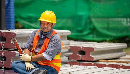 Quadro su tela Portrait of Asian male construction worker holding spirit level sitting on concr