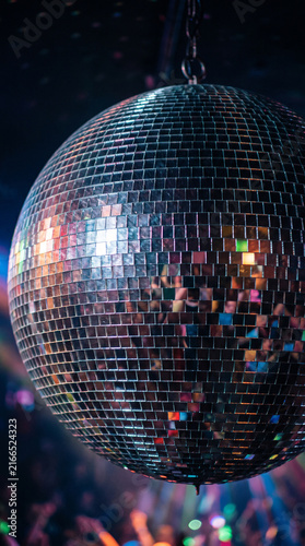 Ultra realistic close-up of a mirrored disco ball reflecting a crowded dance floor, silhouettes of young adults dancing under colorful beams of light 