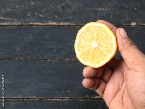 Cuadro en lienzo Hand holding a fresh half sliced yellow lemon fruit against a dark rustic wooden background
