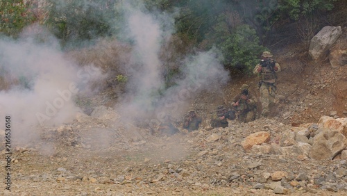 Canvastavla A tactical squad of soldiers in camouflage advances through rocky terrain under the cover of smoke during a high-stakes military training mission or combat operation