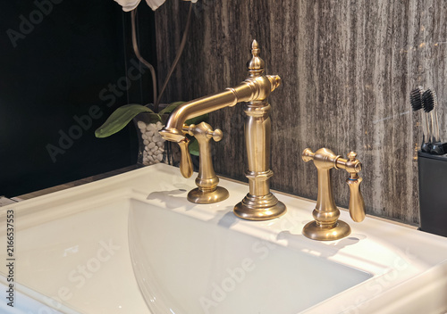 Luxury antique brass double handle mixer faucet installed on white ceramic washbasin with orchid flower and dark slate wall backdrop, targeted for luxury bathroom interior design