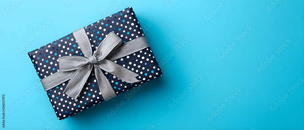 Obraz premium Top view flat lay of blue polka dot wrapped gift box tied with striped ribbon bow isolated on bright cyan background holiday birthday celebration concept