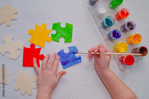 Top view child painting colorful wooden puzzle pieces blue red yellow green paints Creative educational activity Kids learning through art Preschool craft motor skills Autism awareness inclusion conce