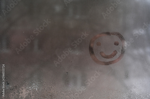 Hand drawn smiley appears on misted window pane with indoor condensation. Positive happy symbol brings optimistic mood to steamy glass surface. Simple creative smiley offers cheerful emotion.