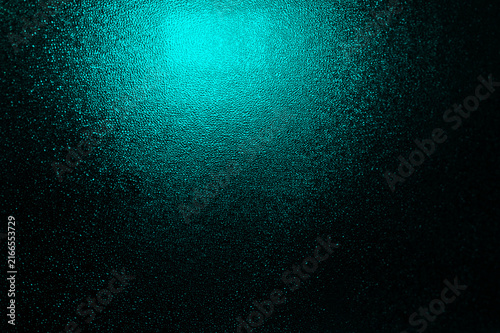 Wet glass texture with turquoise glow creates abstract background featuring moisture particles and dark gradient. Surface pattern futuristic atmosphere, modern design element, creative backdrop
