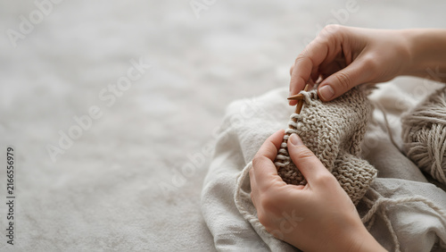 Close-up of hands knitting with generous negative space around, rich tactile textures of yarn and fabric, soft natural light, calm and intimate mood, minimalist commercial framing
