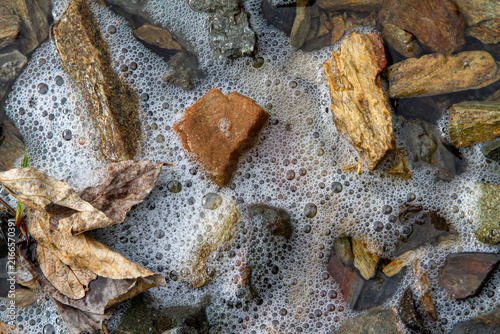 Foto Close-up of foamy water with rocks and fallen leaves on the surface, background,