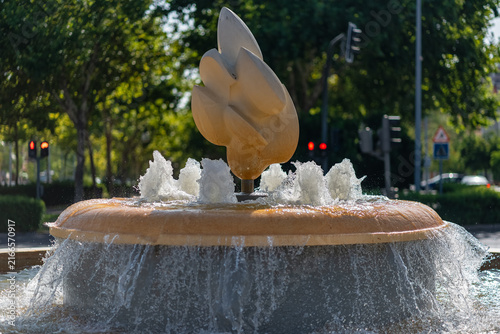Sunlit abstract sculpture surrounded by bubbling water jets in a landscaped urban fountain