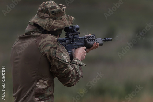Photography A soldier in a wide brimmed bush hat fires his service rifle from the standing position, muzzle smoke drifting into soft green bokeh