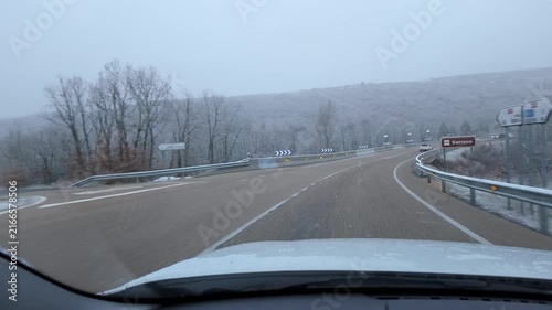 Driving toward a curved highway junction through snow covered woodland during winter snowfall