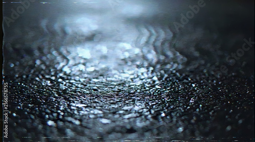 Wet, textured ground reflects blurred lights in a dimly lit environment.