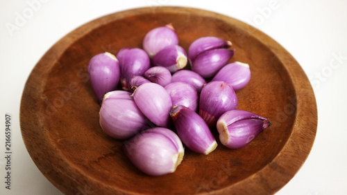 Fresh red shallots are arranged on a rustic wooden plate against a clean white background