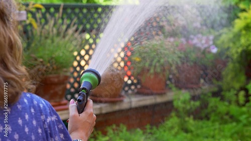 Slow motion close up of woman spraying water across potted plants in a green garden