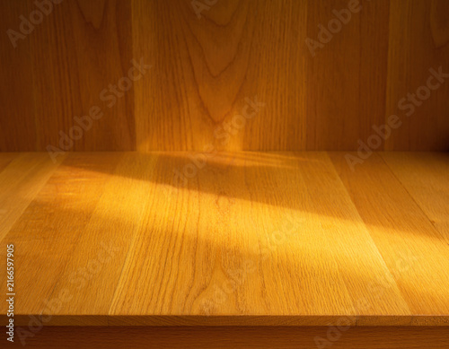 Natural wooden surface and matching background illuminated by warm sunlight casting diagonal light patterns creating a beautiful texture and clean space for product placement