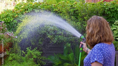 Slow motion woman watering dense garden foliage with a hose and wide fan of water