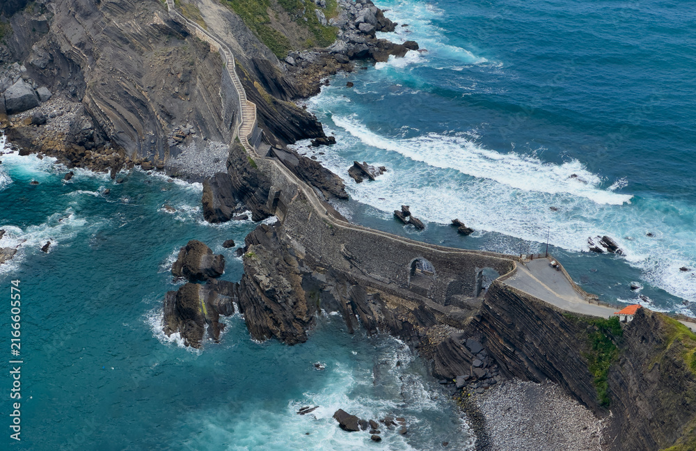 Fototapeta premium serene coastal pathway winding along rocky cliffs near the ocean with a concrete staircase leading to the shore, aerial perspective showcasing nature and architecture in harmony.