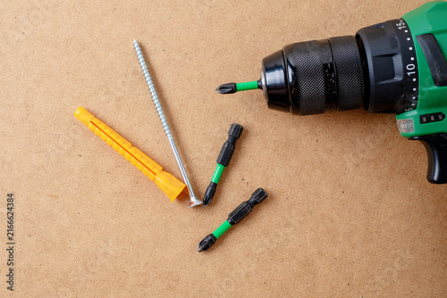 Green cordless drill with bits, screw, and orange dowel