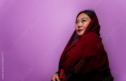 Thoughtful Asian Woman in Red Headscarf Looking Up Against Purple Background