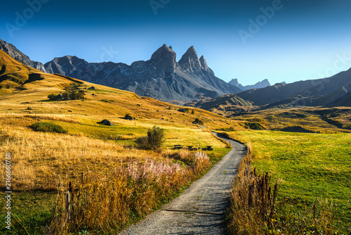 Winding gravel path through alpine valley with Aiguilles d Arves mountain peaks in French Alps during autumn