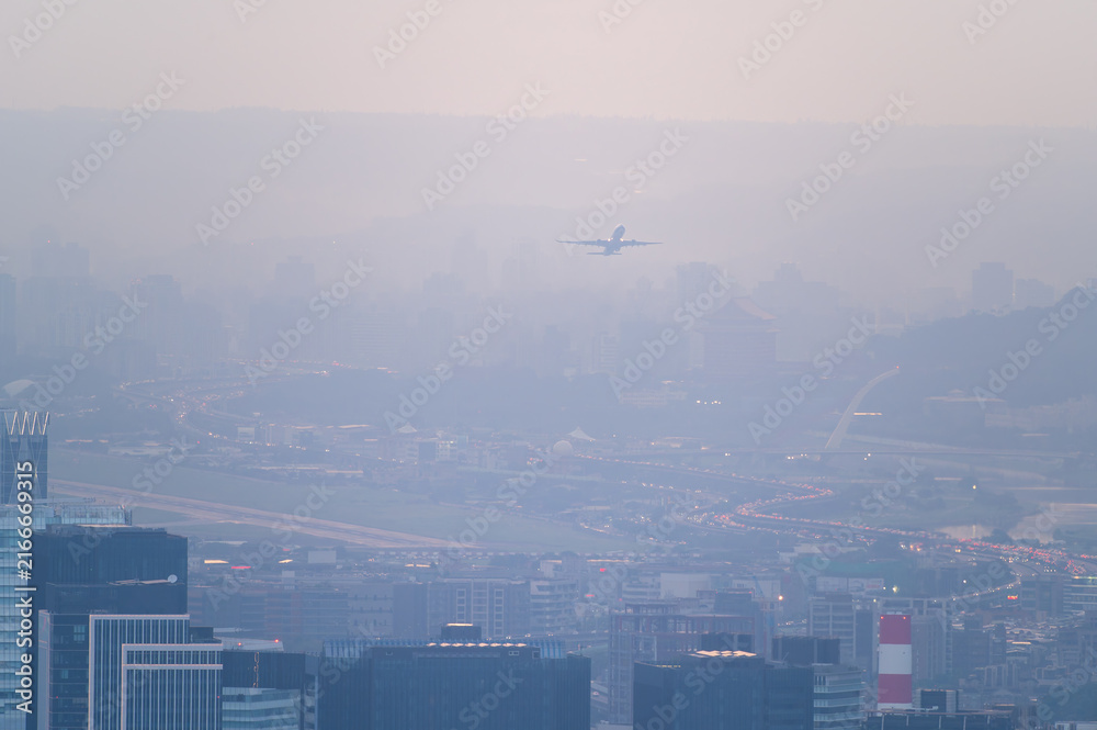 Fototapeta premium An airplane takes off over the hazy urban skyline of Taipei and New Taipei City, Taiwan, viewed from Datian Mountain.