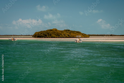 Фотография A small tropical island and a small boat surrounded by ocean and blue sky