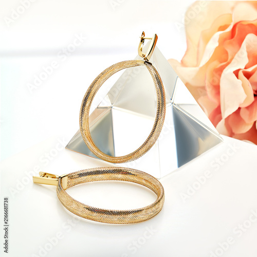 Photography Elegant Golden Hoops Resting on a Reflective Surface Beside a Soft Floral Backgr