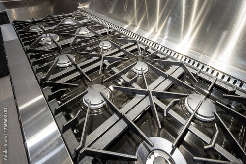 Close-up view of a professional stainless steel gas stove cooktop with heavy-duty black cast iron grates and multiple burners.