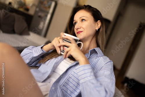 Quadro su tela Woman enjoys drink while sitting on couch in cozy living room during afternoon