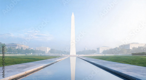 Reflecting pool with tall white obelisk monument at misty morning sunrise