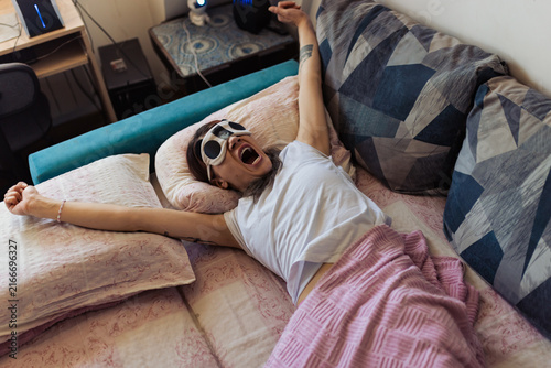 Fotografie Girl sprawls on bed with arms raised and mouth open in surprise inside a room du