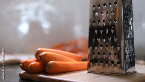 Close up of a metal box grater and peeled carrots prepared for food preparation on a kitchen surface