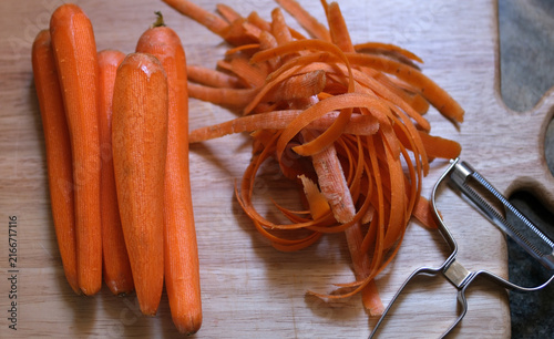 Top view of peeled carrots with vegetable peels and a vegetable peeler on a kitchen surface