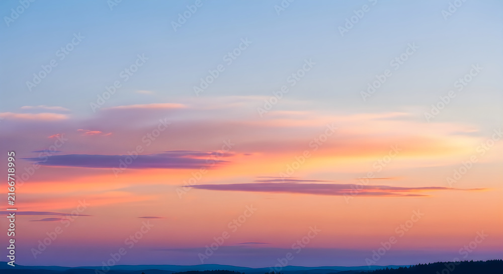 Fototapeta premium Serene sunset sky with soft pink and orange clouds over a distant hazy landscape