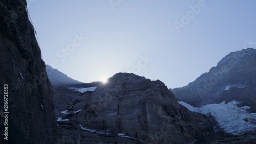Bright sun rising from behind a rocky mountain ridge creating a beautiful lens flare effect. Switzerland