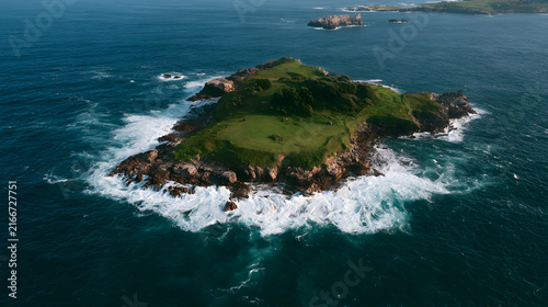 Aerial view of a serene island surrounded by vibrant blue ocean waves, showcasing lush greenery atop rocky terrain.