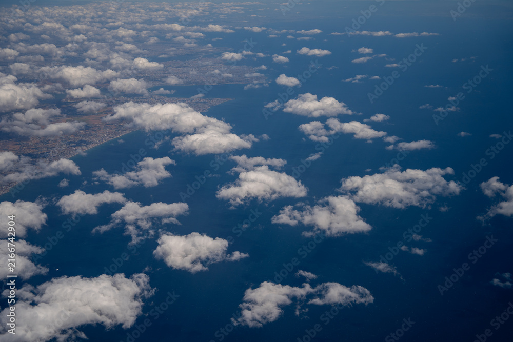 Fototapeta premium White fluffy cumulus clouds scattered over deep blue sea water aerial view. Freedom of travel and aviation transit concept in bright daylight environment.