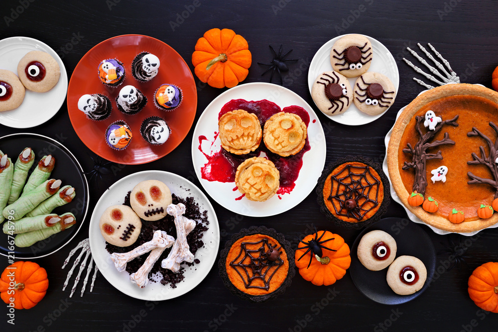 Fototapeta premium Fun Halloween dessert table scene over a black wood background. Overhead view. Variety of cookies, cupcakes and pumpkin and apple tarts and pies.