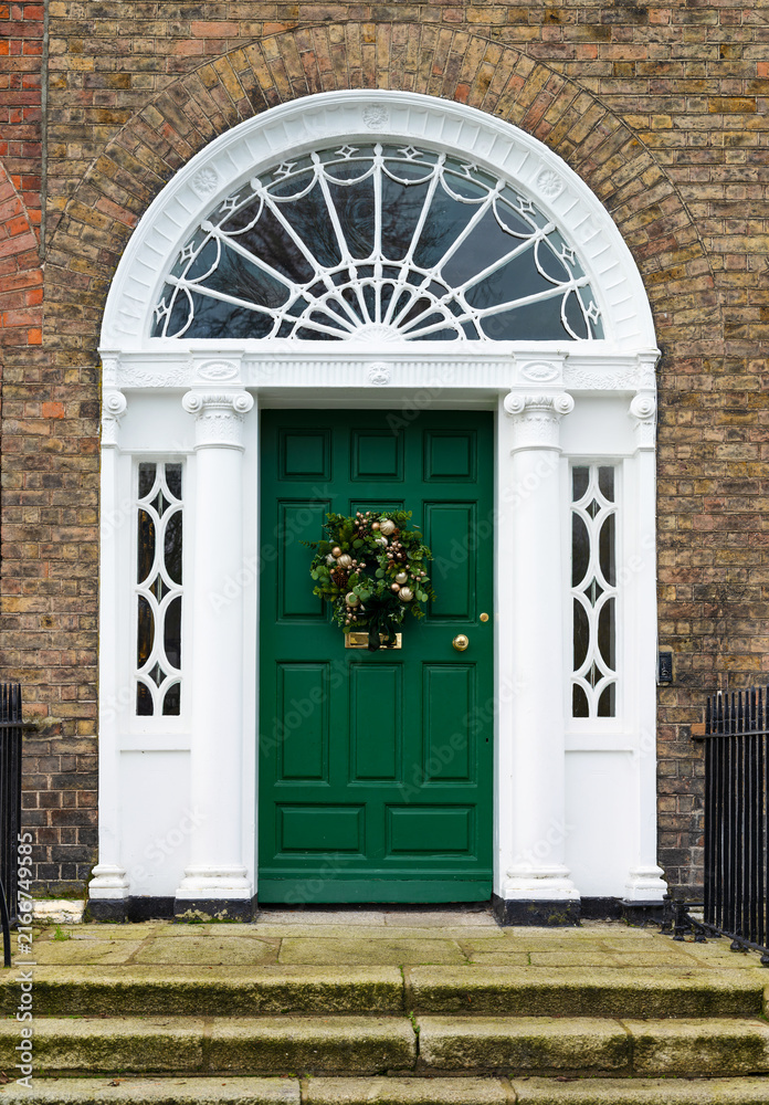 Obraz premium Green Georgian front door decorated for Christmas Holiday season with seasonal wreath. Entrance to house with decorative fanlight and columns. Dublin, Ireland