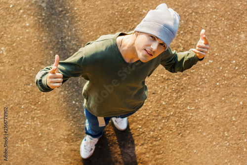 Fotografie Top-down view of a cool young breakdancer in a beanie pointing up at the camera outdoors