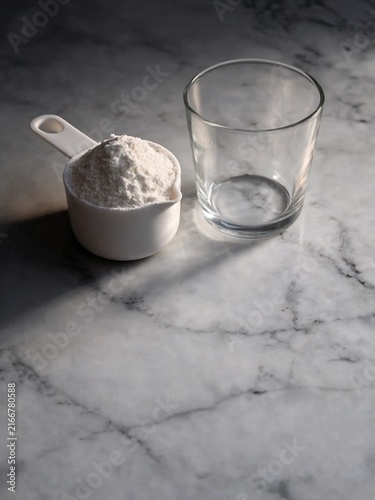 Fine white powder supplement protein scoop beside empty glass on bright marble counter