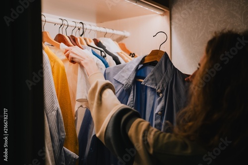 Woman choosing clothes from a wardrobe at home, comparing shirts on hangers while selecting an outfit and organizing her everyday personal style