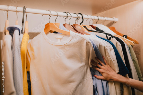Photography Hand browsing clothes on hangers inside a home wardrobe, choosing between shirts