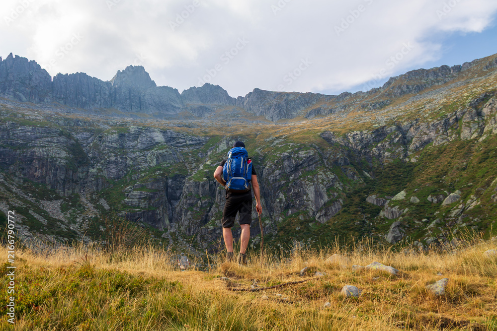 Fototapeta premium Hiker with Backpack Facing Steep Rocky Mountain Range