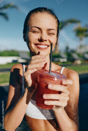 Foto Happy woman outdoors by a pool holds a smoothie, smiling at the camera, bright sun, casual summer vibe, tropical setting, healthy lifestyle, social moment and wellbeing